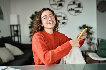 Young happy woman holding smartphone using cellphone modern technology, looking at camera with mobile, checking cell phone app, texting typing messages, browsing internet for shopping sitting at home.