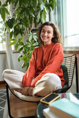 Vertical portrait of smiling cheerful lady chilling in apartment, laughing, feeling relaxed and satisfied. Happy pretty young positive woman sitting on chair relaxing at home looking at camera.