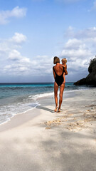 Young mother holding her blond son in arms, while walking back to the camera on empty Caribbean beach  inCuraçao. Family traveling, traveling with kids, childhood, parenting