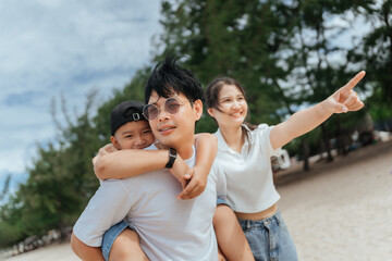 Family enjoys sunny day on the beach with child on father's back pointing at the distance