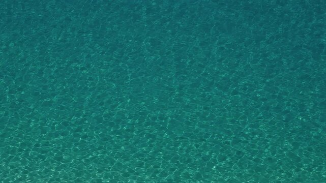Crystal clear turquoise water surface with gentle ripples forming a mesmerizing pattern in Tropea, Calabria, Italy
