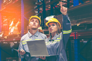 Two logistic factory  workers, man and woman in a warehouse, check stocks and reviewing data on a...