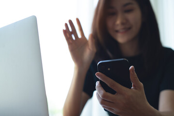 Happy asian business woman using smartphone for video call, waving hand and talking to colleagues during online meeting, remote work from coffee shop, video conference, close up