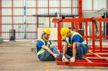 A construction worker holds his injured foot while his coworker kneels beside him and helps him.