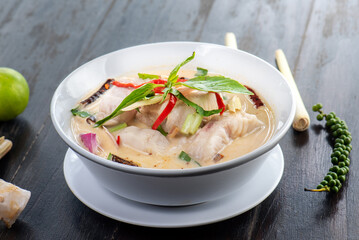 A bowl of Tom Yum soup with fish, vegetables, and spices.