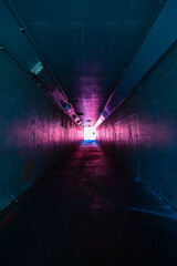 Long dark empty tunnel walkway with light at the end.
