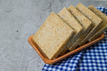 Close up view of whole wheat sliced bread on long wooden plate with napkin. grey or gray cement as background. blue, white. copy space, free, empty, negative.