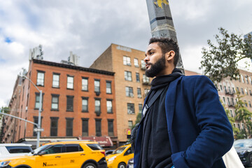 black man contemplative wearing blue coat with yellow taxis at the background in New York City,...