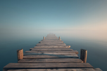 Fototapeta premium Minimal Wooden Pier Leading into Calm Foggy Ocean with Centered Vanishing Point