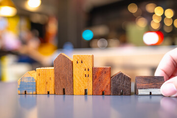 Hand choosing mini wood house model from model on wood table, Planning to buy property. Choose what's the best. A symbol for construction ,ecology, loan concepts