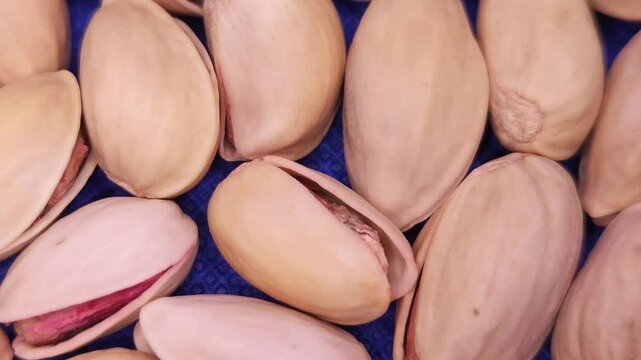 Video footage in slow motion, A pile of roasted and salted pistachios, revealing their naturally cracked shells and vibrant green interiors. Food Background