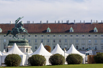 
a large, historic building with a red roof and many windows, in the foreground is a row of white...