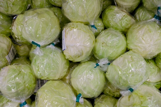 Plastic waste concept in supermarket. Fresh cabbages individually wrapped in produce section, pre-packed in plastic. This method to extend shelf life of fresh produce leads to plastic pollution.