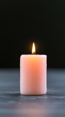 A single, illuminated, light pink candle on a dark surface