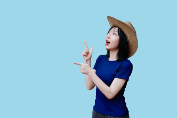 Exciting female pointing enthusiastically while wearing a straw hat and a blue shirt against a...