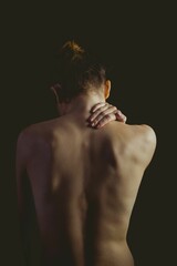 Woman is showing bare back in dark studio portrait, highlighting spine ridges and bun
