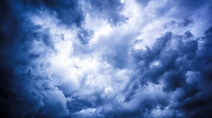 Dramatic sky filled with dense, textured clouds in deep blue and gray tones, creating a moody atmosphere with a break of soft white light filtering through.