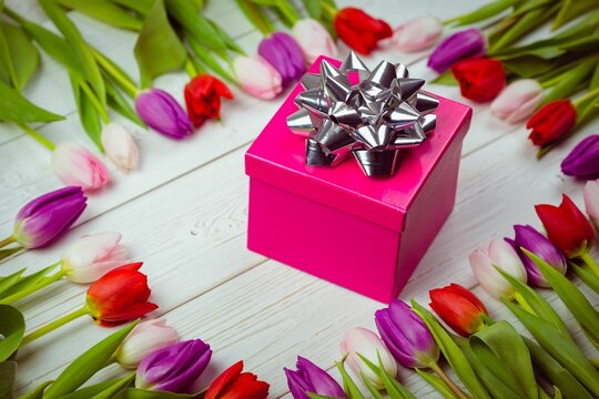 Fototapeta Flat-design pink gift box is resting on white wooden table with silver bow and tulip wreath