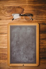 Obraz premium Chalkboard with wood frame and black-rimmed eyeglasses are resting on wood table in flat design