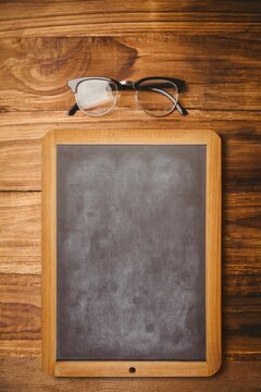 Fototapeta Chalkboard with wood frame and black-rimmed eyeglasses are resting on wood table in flat design