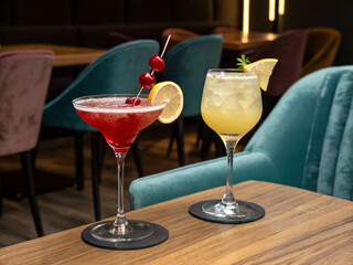 Two colorful, refreshing cocktails beautifully presented on a wooden table in a trendy lounge.