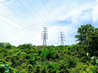 High-voltage electricity pole standing tall on a green hillside, surrounded by trees and set...
