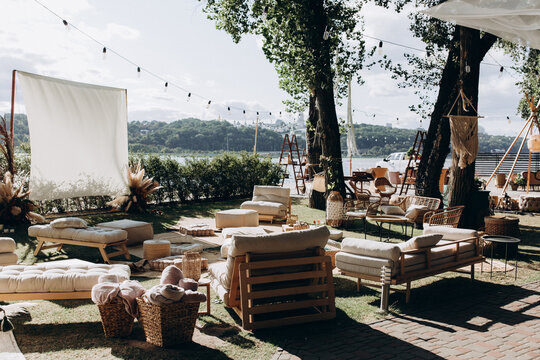 Stylish outdoor boho-style lounge setup near a lake with cozy seating, natural decor, and warm sunlight &mdash; perfect for events or relaxation.