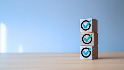 A minimalist photo shows three identical wooden blocks stacked on a light desk with turquoise checkmarks against a soft gray background