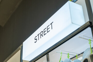 Close-up side angle of an illuminated white retail sign with the word "STREET" above a footwear display in a modern store interior.