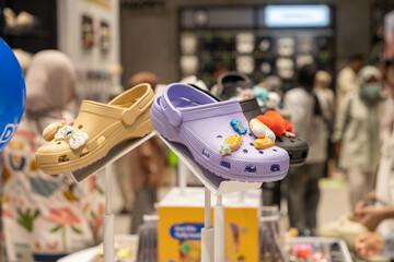 Colorful rubber clogs with decorative charms displayed on a store shelf, attracting shoppers in a crowded retail setting. Fun and playful footwear fashion in a modern shopping environme