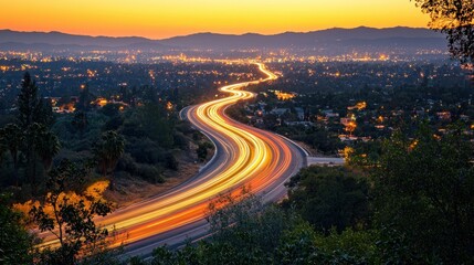 Highway at sunset, winding through valley.  City lights below
