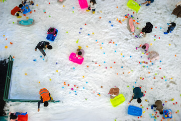 Top-down view of children playing in artificial snow with colorful toys and sleds indoors, capturing joyful winter fun, family entertainment, and vibrant childhood activity in a snowy play area.
