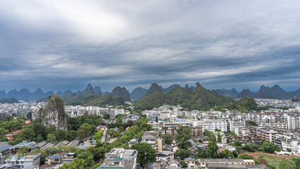 Panorama of a modern city. Lots of buildings, green trees. There is a pavilion on top of a high sheer cliff. Silhouettes of mountains on the horizon. Clouds, sky. China.Guilin.View from the Fubo Hill 
