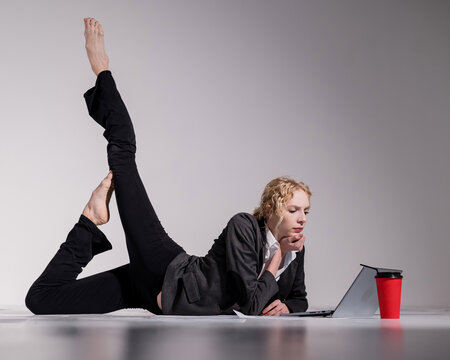 A ballerina dressed in a business suit poses for a laptop and drinks coffee. Flexible woman works at the computer