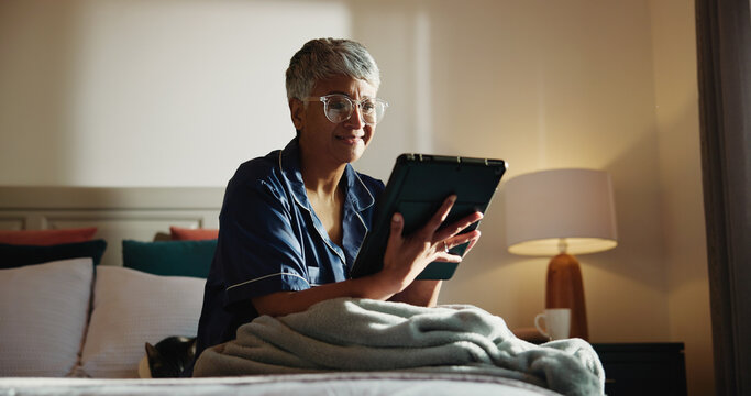 Home, tablet and senior woman in bedroom, internet and online reading for news report. Pensioner, apartment and elderly person with tech, digital app and social media with email, relax and chatting - Powered by Adobe
