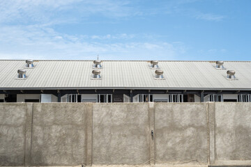 Concrete wall in front of a modern industrial building with metal roof and turbine ventilators,...