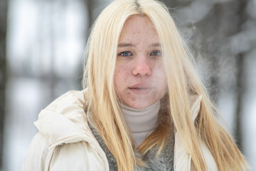 Portrait of a young beautiful blonde girl in light clothes outdoors in winter.