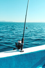 Fishing pole ready for action on a boat in the open sea with mountains behind