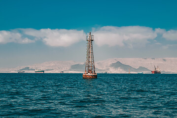 Wide view of a navigational beacon in the sea with cargo ships and mountains