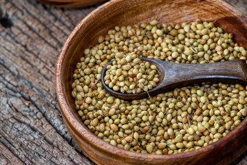 Spice coriander (Coriandrum sativum) seeds in wooden bowl and spoon on wooden background. Indian cuisine, ayurveda