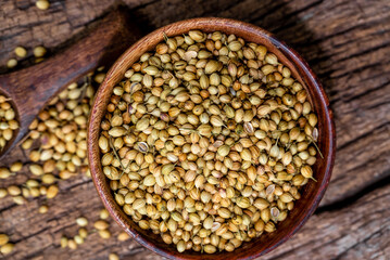 Spice coriander (Coriandrum sativum) seeds in wooden bowl and spoon on wooden background. Indian...
