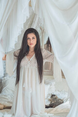 A brunette woman stands quietly in the morning light, wrapped in a sheer white vintage gown, ...