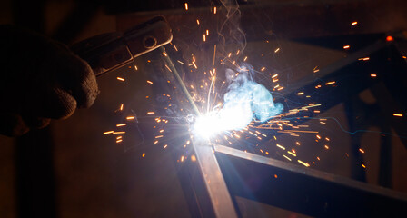 A man is welding a piece of metal with a bright blue flame