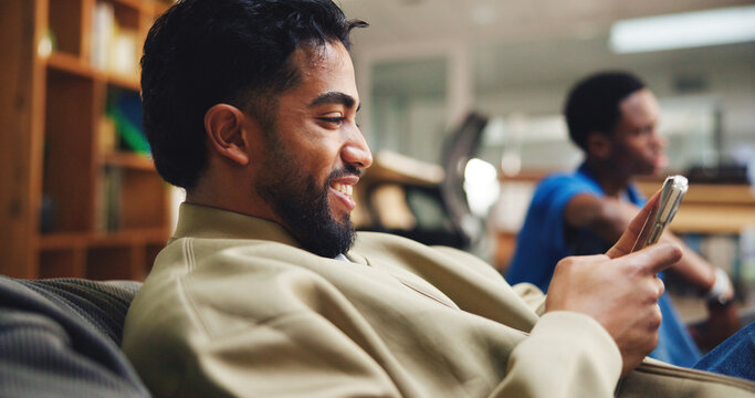 Fototapeta Phone, man and student relaxing in library with networking, connectivity or contact on mobile app. Happy, bean bag and male person with cellphone for texting with communication online on campus.