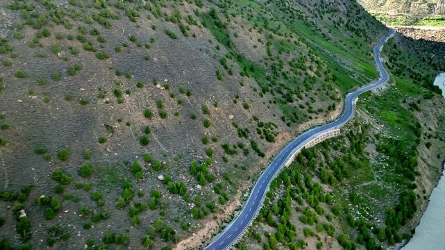 4K HQ Aerial drone footage of curvy Manali Leh Highway winding through green, rocky, snowy mountain terrain beside a river. Stunning high-altitude scenery showcasing Himalayan wilderness in motion.