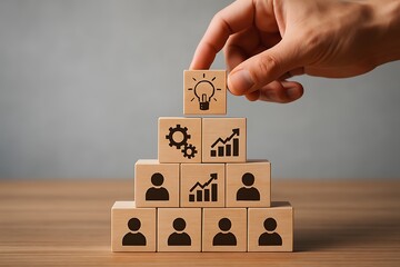 Hand placing an idea block atop a pyramid of wooden blocks symbolizing business team growth.