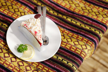 Homemade fresh strawberry cheese cake with lemon piece in white dish on Thai native pattern tablecloth in natural sunlight in tropical cafe