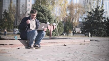 Man working remotely outdoors, drinking coffee and using laptop in city park