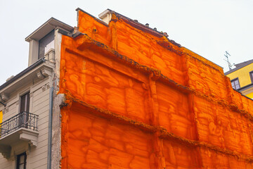 Building with a section of its facade covered in orange insulation material, during renovation or...