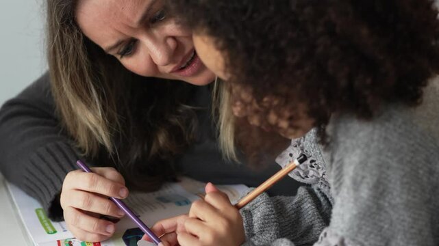 Caucasian mother and African American daughter studying at home, doing homework in cosy white room. Parent teach, child school girl learn knowledge, write exercise read book. Education for children